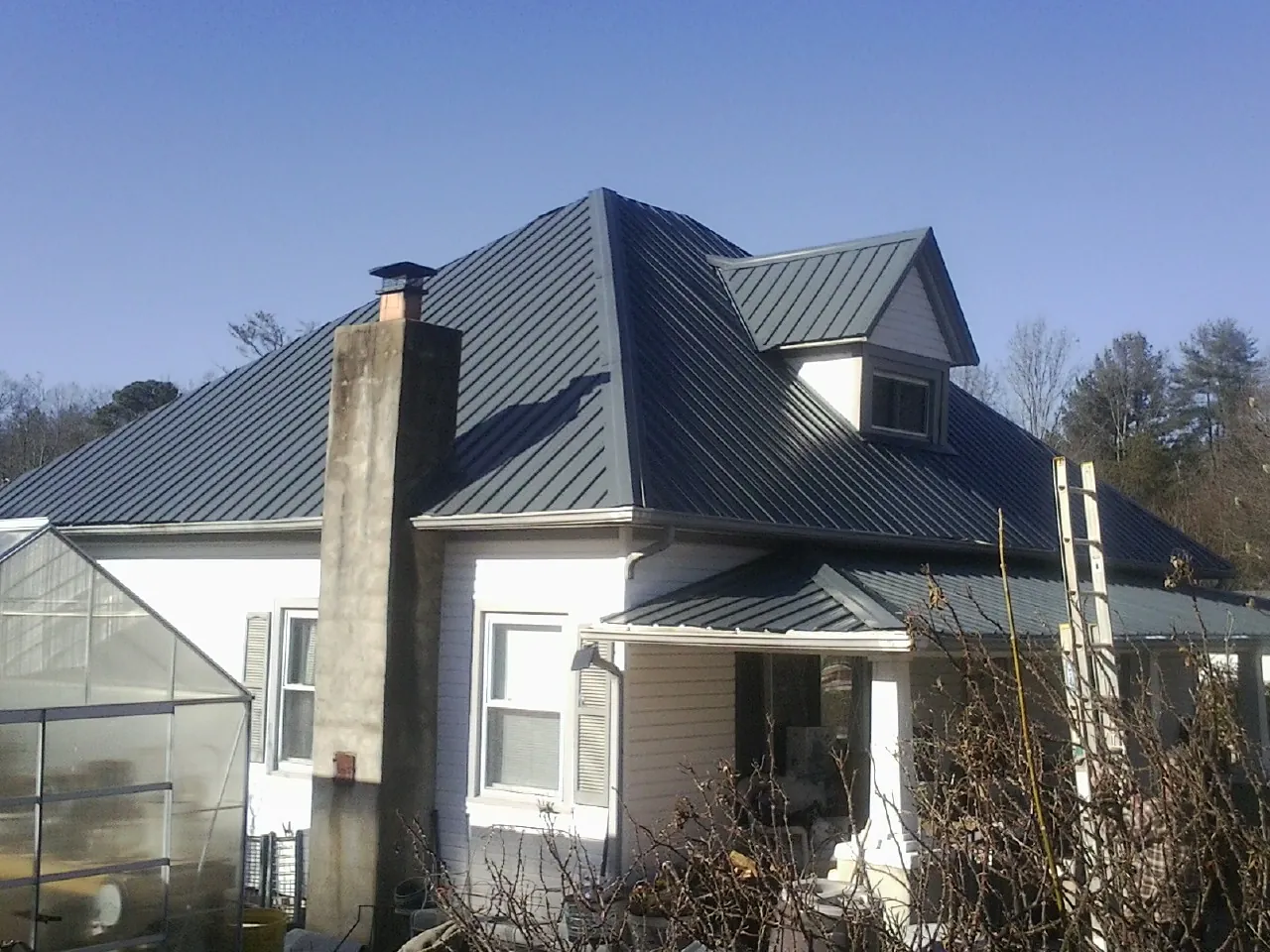 Dark blue standing seam metal roof on a white farmhouse with dormer — Slate & Tile Roof Repair by Roofing Brothers in Ennis