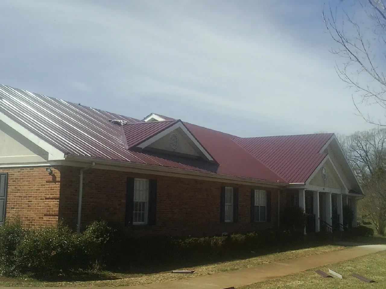 Red metal roof with gabled entries on a long brick building, from a Hail Damage Roof Repair job in Ennis