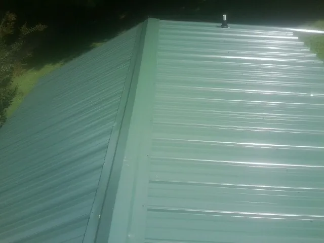 New green metal panels meeting at the ridge of a roof — Flat Roof Repair work by our crew in Ennis