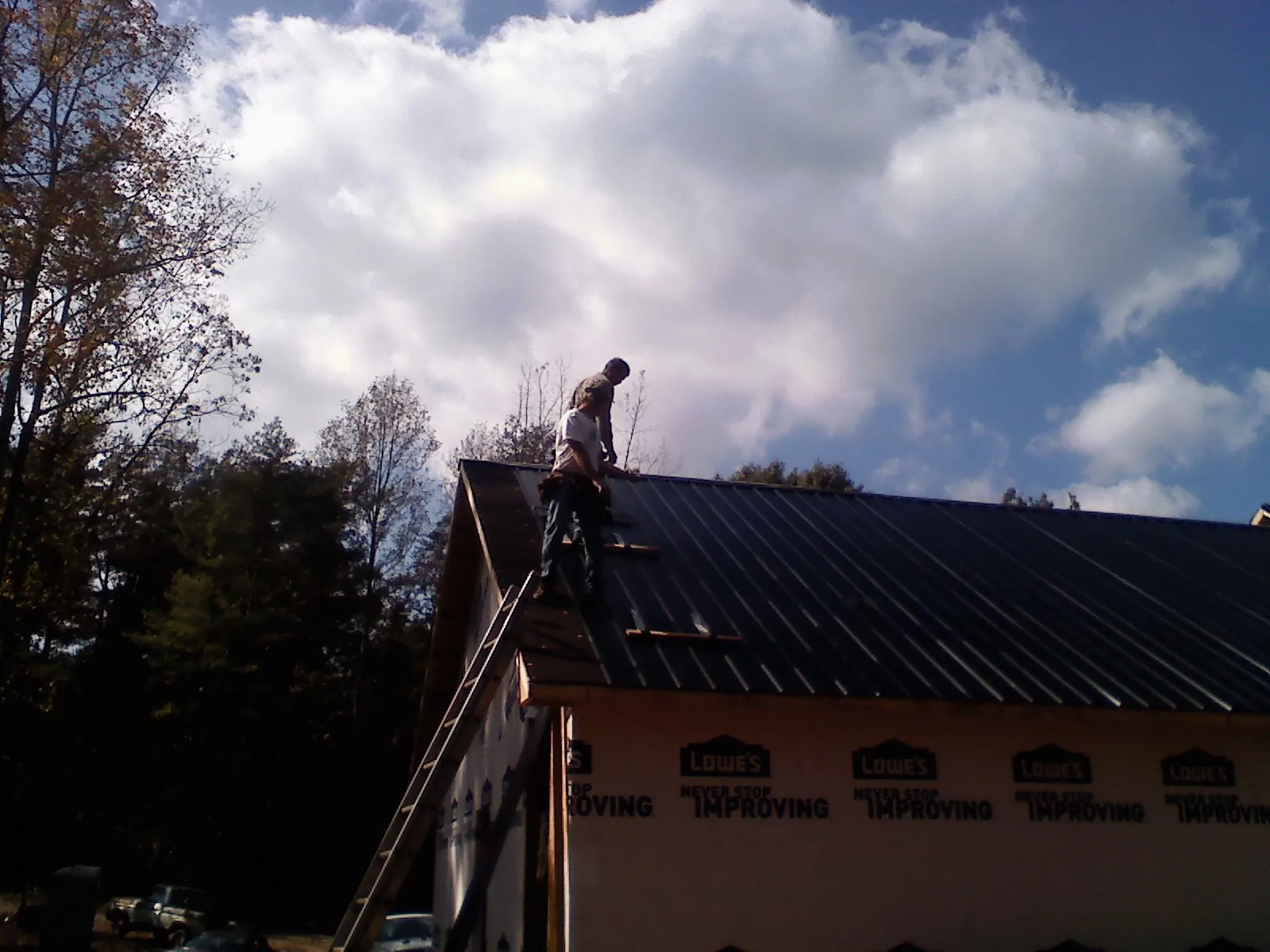Roofer fastening dark metal panels high against a cloudy sky, from a Roof Inspection job in Ennis