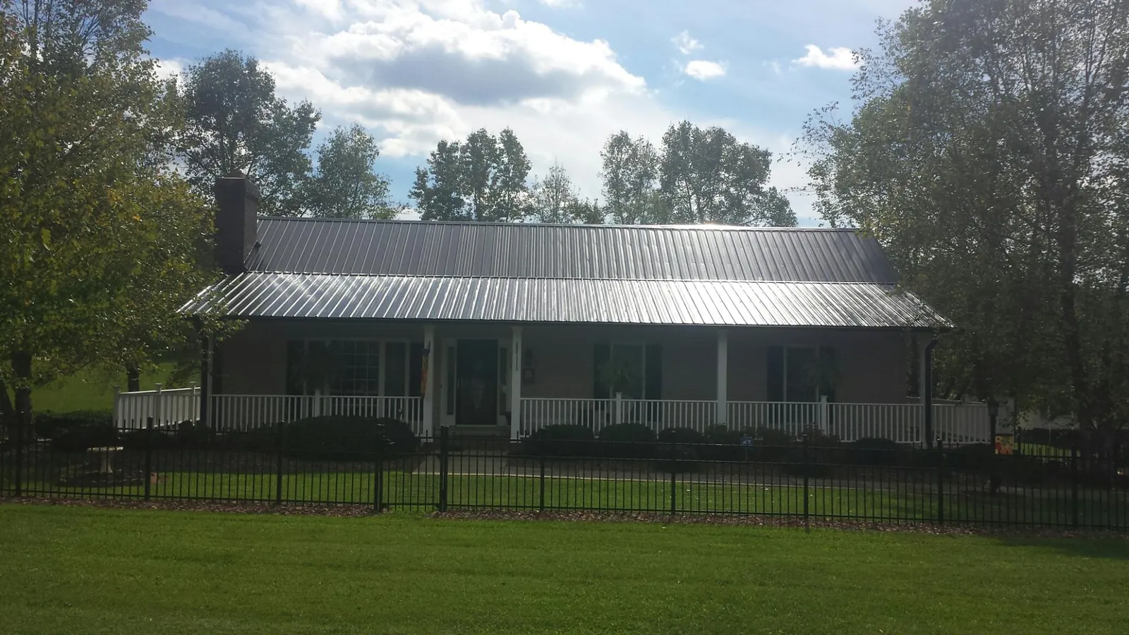 Gray metal roof on a brick ranch with a full width front porch — Gutter Guard Installation work by our crew in Ennis